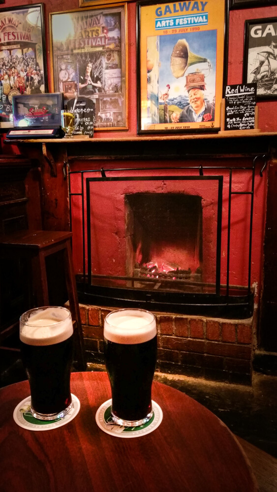 Ireland Galway Tigh Neachtain pub with two pints of Guinness in front of fireplace